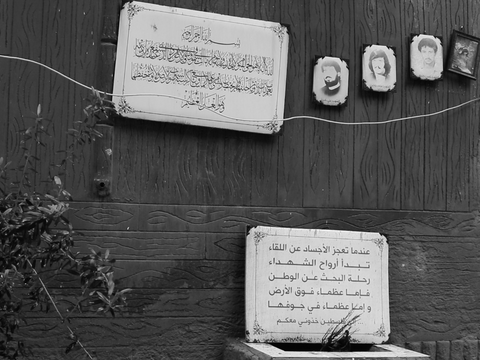 صور الشهداء الأربعة: حسن دغمان ومحمد روبين (أبو شادي) وعلي خبيزة، تجاورها آية الكرسي مطبوعة فوق قبر جماعي، وفوقه لوحة تحمل وصية كُتِبَ فيها: "عندما تعجز الأجساد عن اللقاء، تبدأ أرواح الشهداء رحلة البحث عن الوطن، فإما عظماء فوق الأرض وإما عظماء في جوفها، إلى فلسطين خذوني معكم". برج البراجنة، لبنان. ٤ شباط، ٢٠٢٤. (حَنين عامل، مصدر عام)
