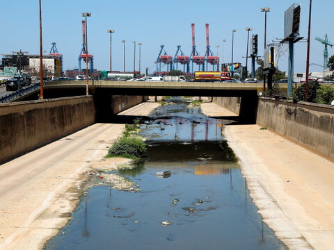 A car bridge stretches over the Beirut River, where the water has slowed to a trickle and appears green-blue from the pollution. 