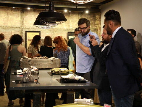 A group of people view small sculptural installations and historical documents at an indoor exhibition.