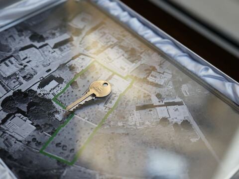 A single key is placed over a faded aerial photograph showing the ruins of a destroyed home.