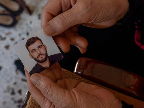 An older woman’s hands hold a passport photo of a young man.