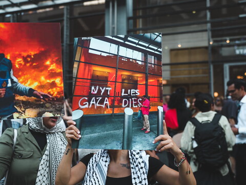 People hold up posters and signs at a protest. The poster in the center of the image is a photo of martyred Al Jazeera journalist Anas al-Sharif, killed by Israel on August 10, 2025. Next to it is a poster that reads: "NYT LIES, GAZA DIES"