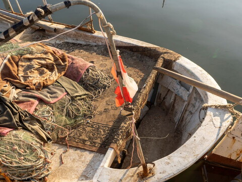 Rugs and fishing nets are piled high on a small boat.