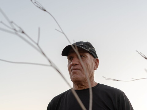  A man wearing a black cap and shirt stands among dry branches under a pale sky.