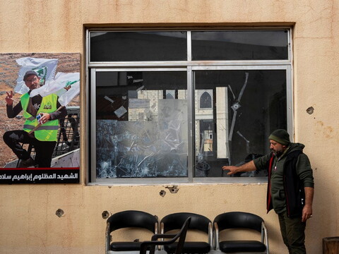 A man points to a bullet-riddled municipality building, with a photo of a martyr  hanging next to the damage.
