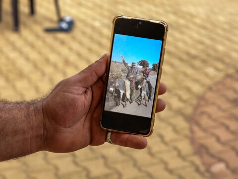 A hand holding a cellphone showing a photo of two men riding a donkey, Hisham Hassan and his great-uncle Ibrahim Salameh, in Blida