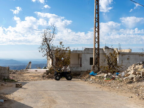 Children riding ATVs through a destroyed area in Kfarshouba, with damaged buildings visible around them.
