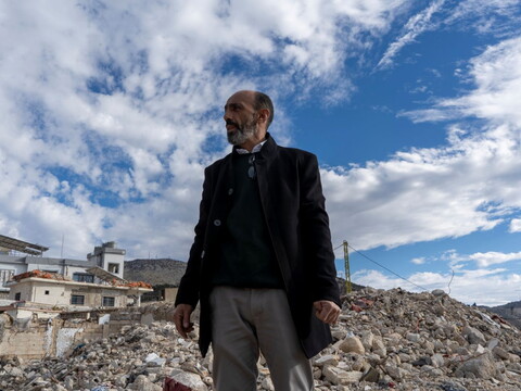 Man standing amidst rubble, with two Israeli military posts visible in the background.