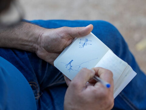 Man drawing a sketch of children and a drone in a notebook.