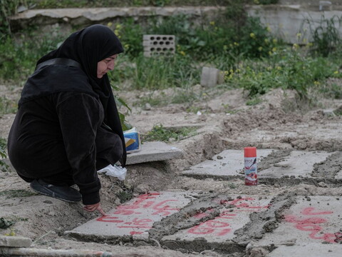 A woman in a black headscarf crouches by a grave at a mass cemetery in Said. 