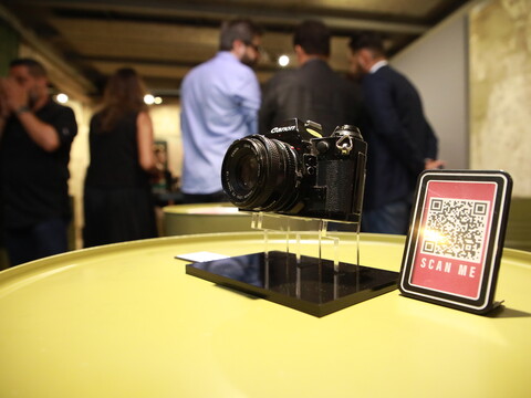 A black camera is displayed on a platform beside a sign with a QR code.