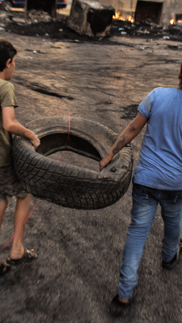 Two young boys carry a tire at a roadblock reinforced by burning dumpsters. Beirut, Lebanon. October 18, 2019. (Mouran Mattar/Fawra)