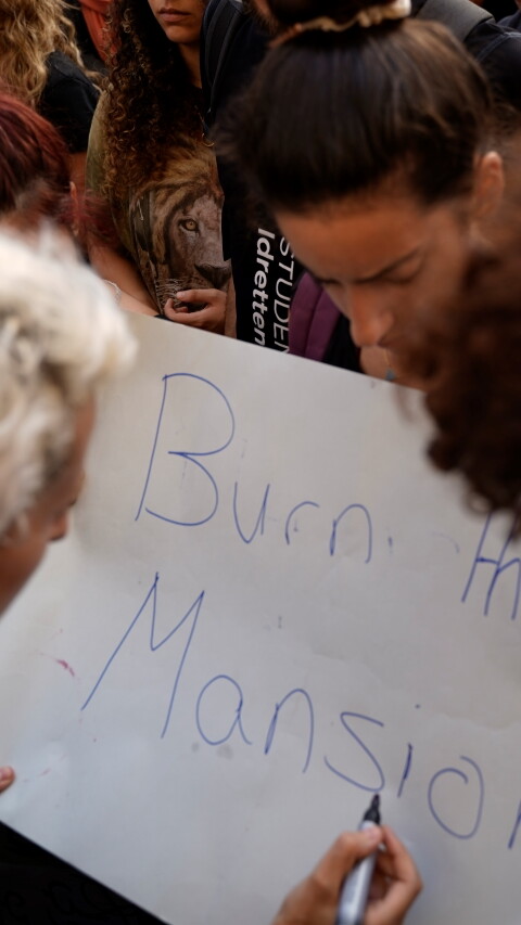 Three protesters hold a sign in Riad al-Solh Square that reads, “burn their mansions." Beirut. Lebanon. October 18, 2019. (Mohamad Cheblak/The Public Source)