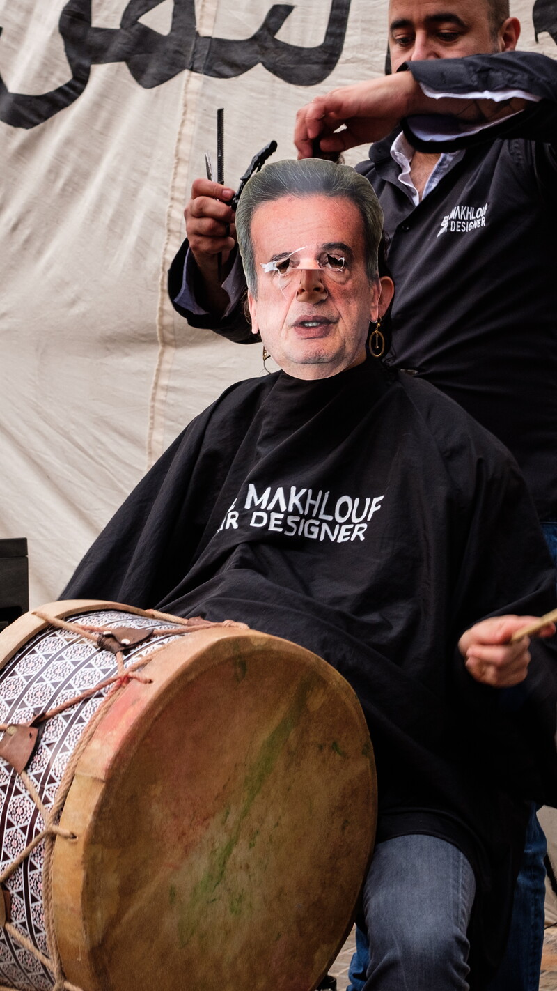 A protester wears a mask depicting central bank governor Riad Salameh’s face while getting a “haircut” in front of the Central Bank.