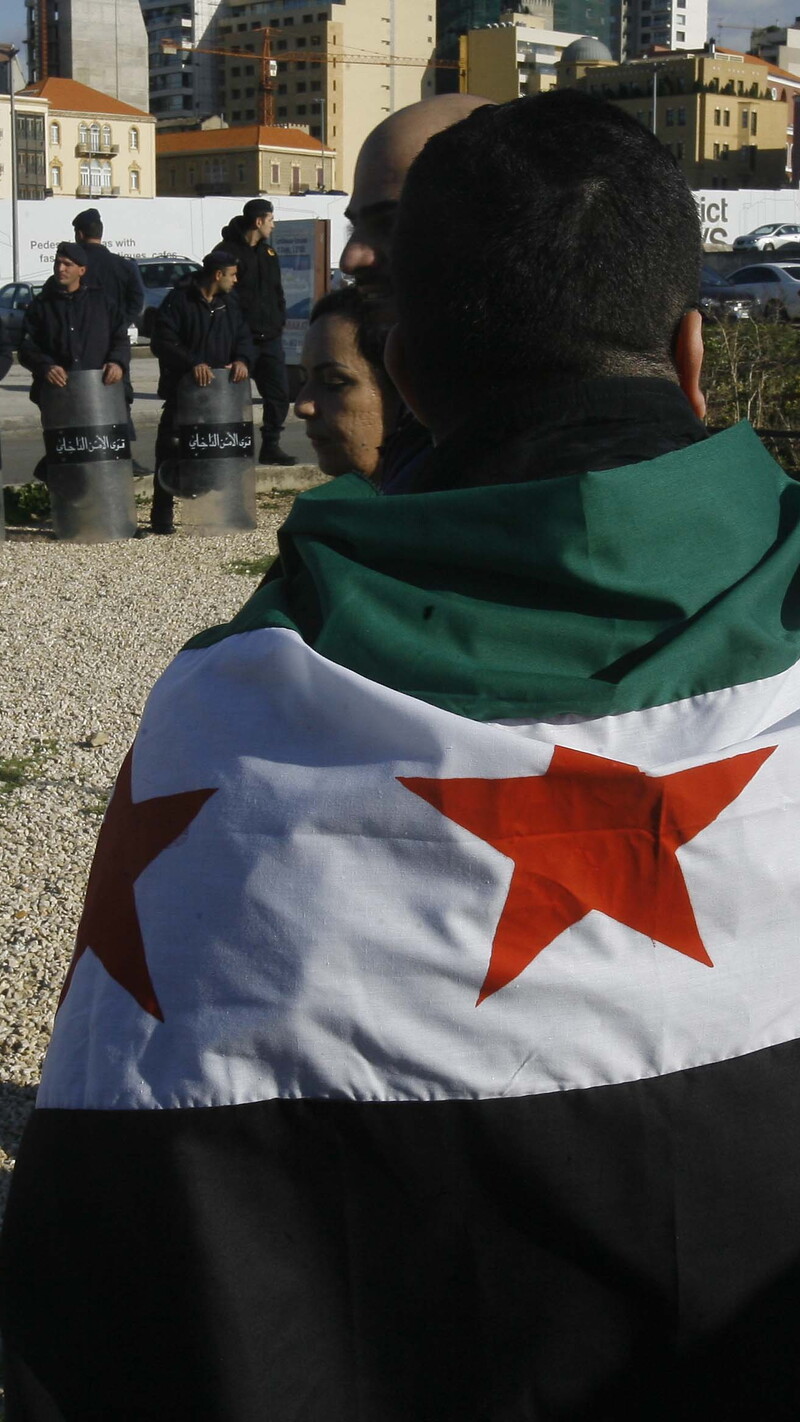 Supporters of the 2011 Syrian uprising, draped in the Syrian opposition flag, gather to commemorate its first anniversary, as members of Lebanon’s Internal Security Forces watch in relaxed shield formation. Martyrs’ Square, Beirut, Lebanon. March 17, 2012. (Marwan Tahtah/The Public Source)