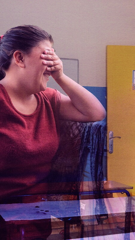 A composite of two images: a girl covering her eyes and looking away with a shy smile on her face in the foreground, with a classroom in the background.