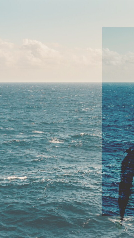 Image of the Mediterranean sea in the background, and a young man in the foreground.