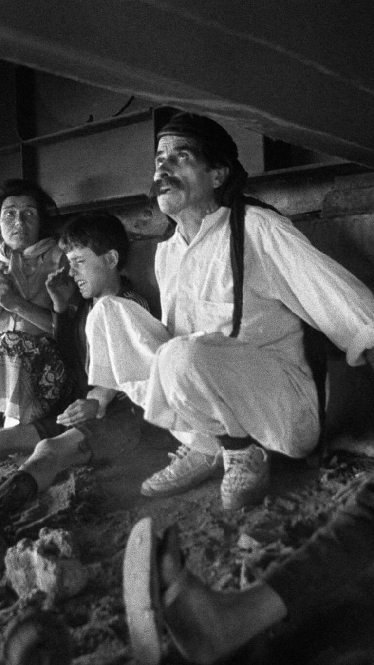 A terrified family taking refuge from shelling under a metallic bridge.