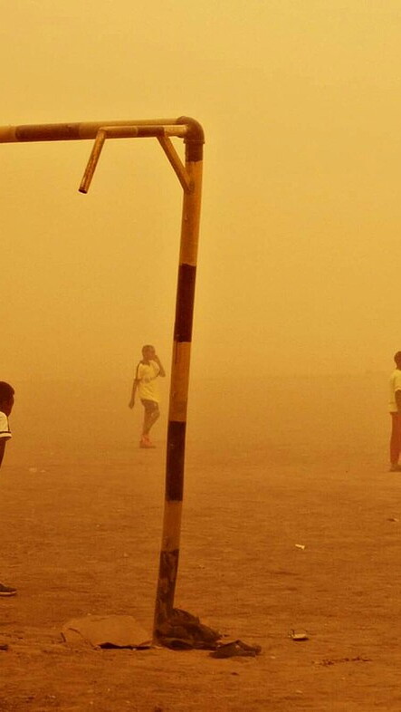 Kids playing football on the sand in the middle of a sandstorm that colors the entire photo golden-yellow.
