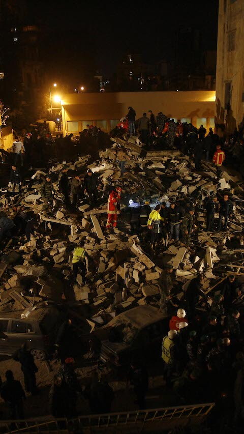 First responders search the ruins of a collapsed building at night.