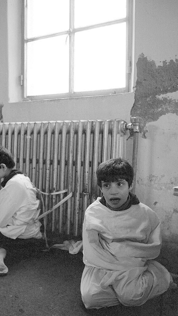 A black and white photograph showing two children fettered to a radiator at the psychiatric hospital of Deir El-Salib in Deir El-Qamar, Lebanon.