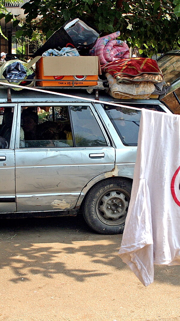 A young man drives a car loaded with his belongings past a park. 