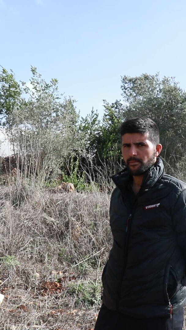 Man wearing black standing in front of his farm in the border town of Dhayra, south Lebanon. He is surrounded by burnt trees and grass impacted by Israel's White Phosphorus attacks. 