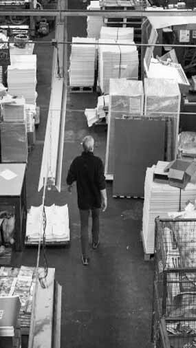 A person walks through a warehouse filled with stacks of paper, boxes, and various materials.
