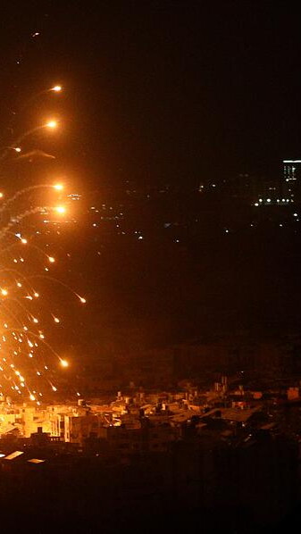 A nighttime airstrike causes an explosion over a dark town.