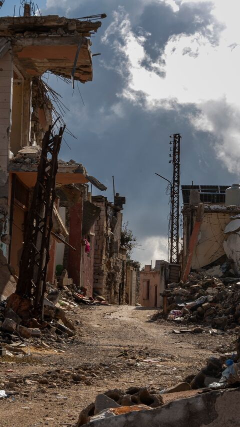 Rubble-lined street between heavily damaged buildings in the village of Blida, south Lebanon, with collapsed concrete and exposed steel.