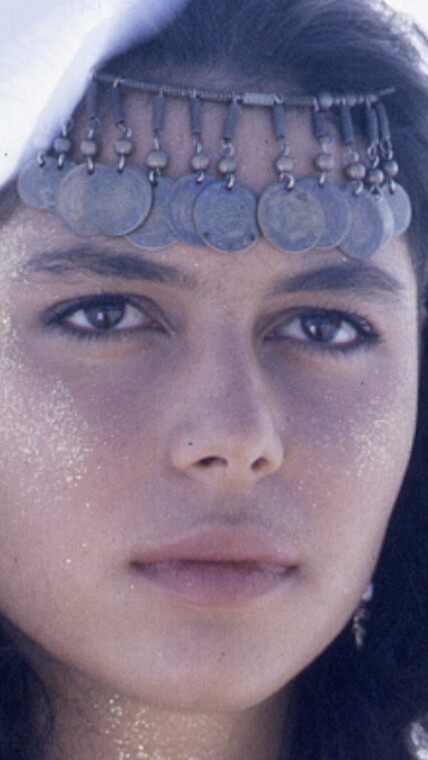 Close up of a woman in headdress and glitter staring into the distance.