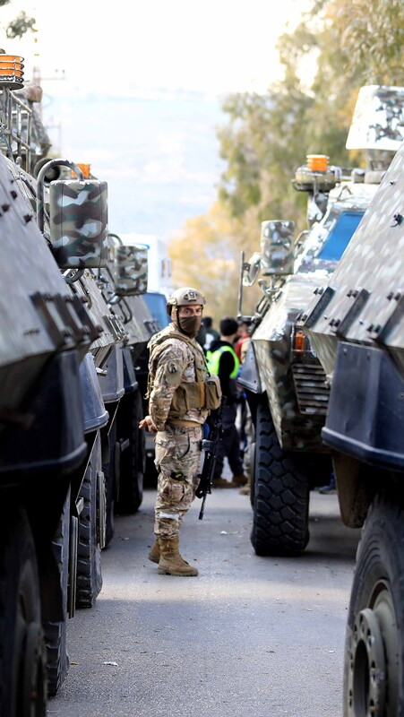 A soldier stands between military vehicles on a street, conveying tension and readiness.