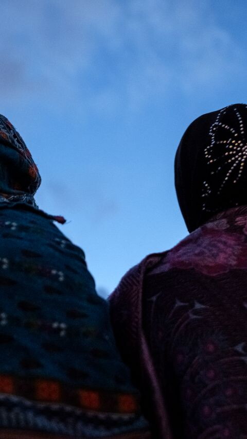 Two women wearing hijab stand under a clear blue sky.