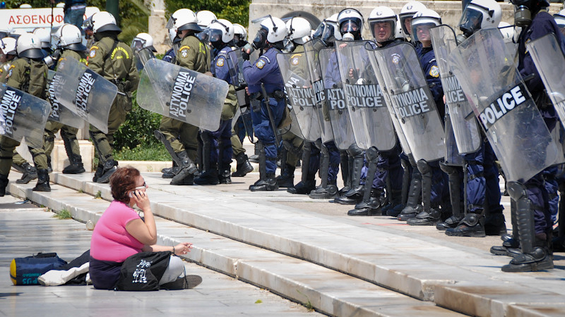 متظاهرة تجلس أمام الشرطة اليونانية خلال اعتصام ضد التقشف في أثينا. ١١ أيار ٢٠١١. (واتسونز واندرينغذ، المشاع الإبداعي)