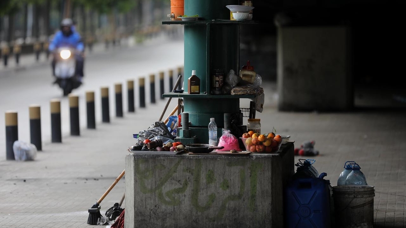 Bruised fruits and kitchen utensils are laid around the green metal column of the Fiat bridge in Beirut.