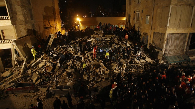 First responders search the ruins of a collapsed building at night.