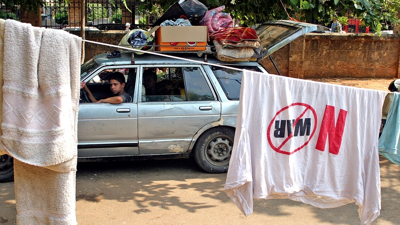 A young man drives a car loaded with his belongings past a park. 