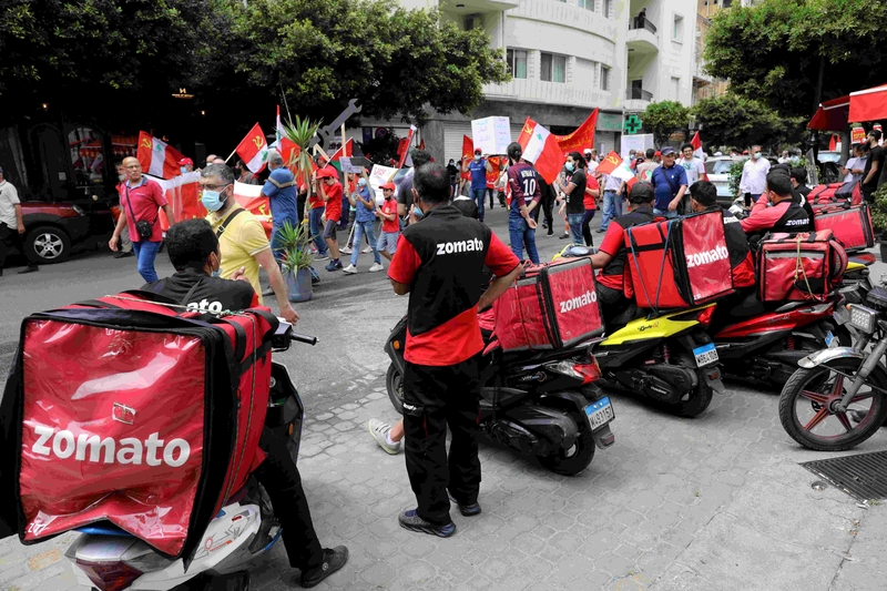 A May Day march takes place. The Lebanese Communist Party flag is raised by some protestors. Zomato drivers watch from the sidelines.