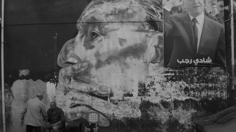 On the left, two old men chat before a mural by Tripoli’s visual artist Ali El Rafei, close to Al Shiraa Square in El Mina. At the top right corner, a picture of politician Ashraf Rifi covers part of the mural.