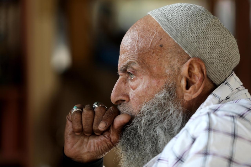 A side profile of an old pensive man. Holding his upper lip with his hand.