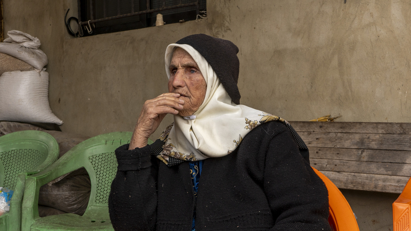 Hajjeh Nasra sitting on a plastic chair, looking at the funeral procession passing by.