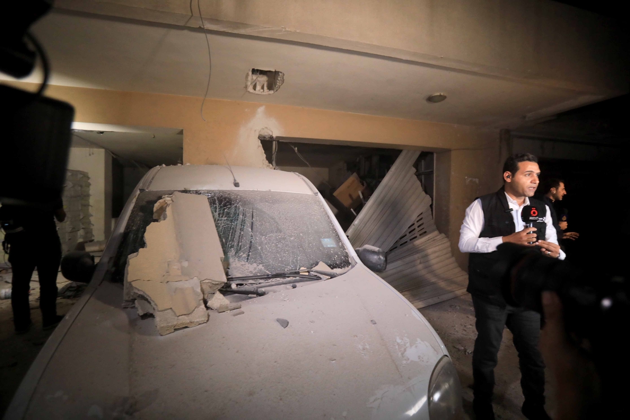 Reporter stands next to blast-damaged car