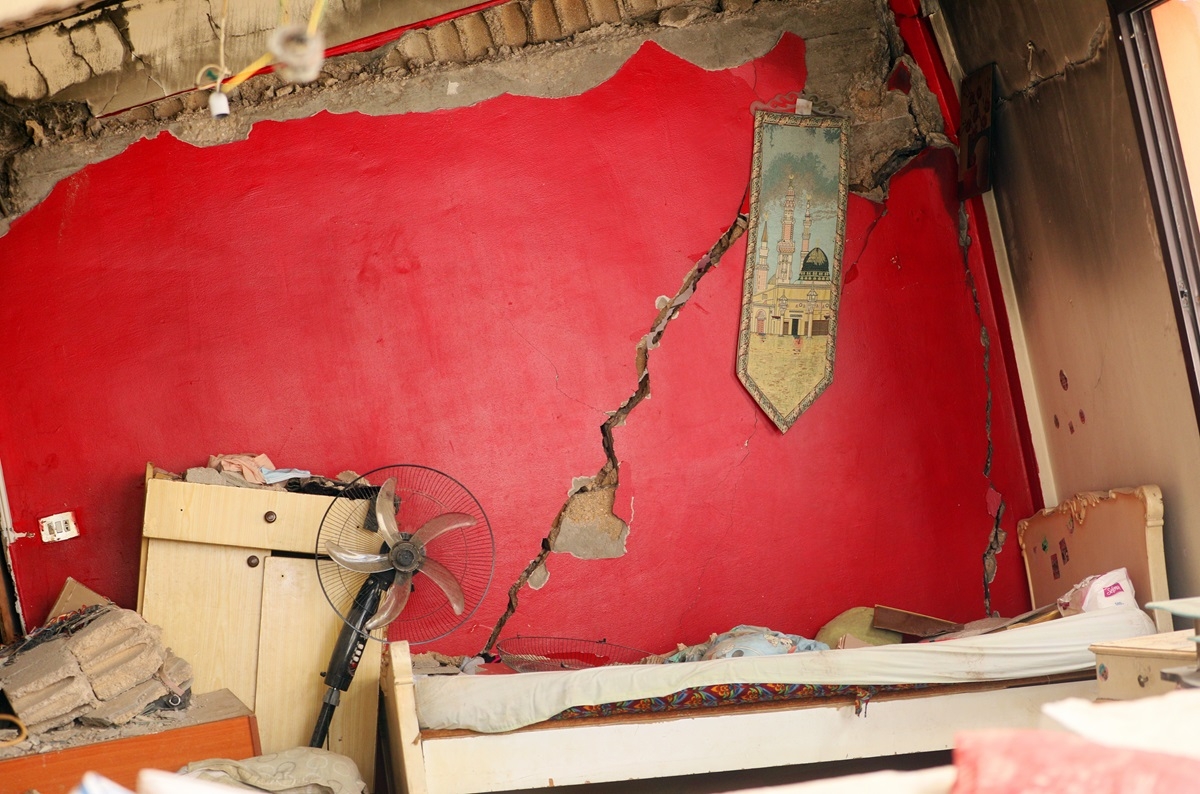 A collapsing red wall and destroyed furniture. A piece of tapestry showing the al-Aqsa Mosque still hangs on the red wall.