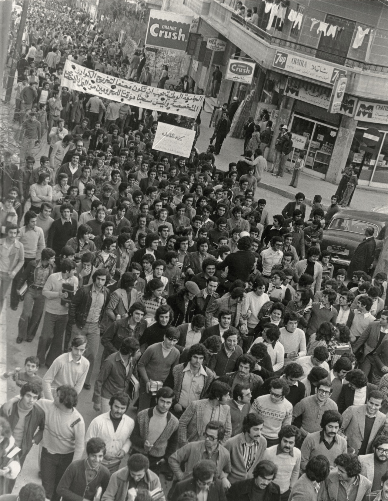 A photo showing a large group of students: a student march. One sign reads: “The National University should be a factory that produces specialized cadres, not a temporary prison for those deprived of work and specialization.” On a smaller sign: “Haigazian College.”