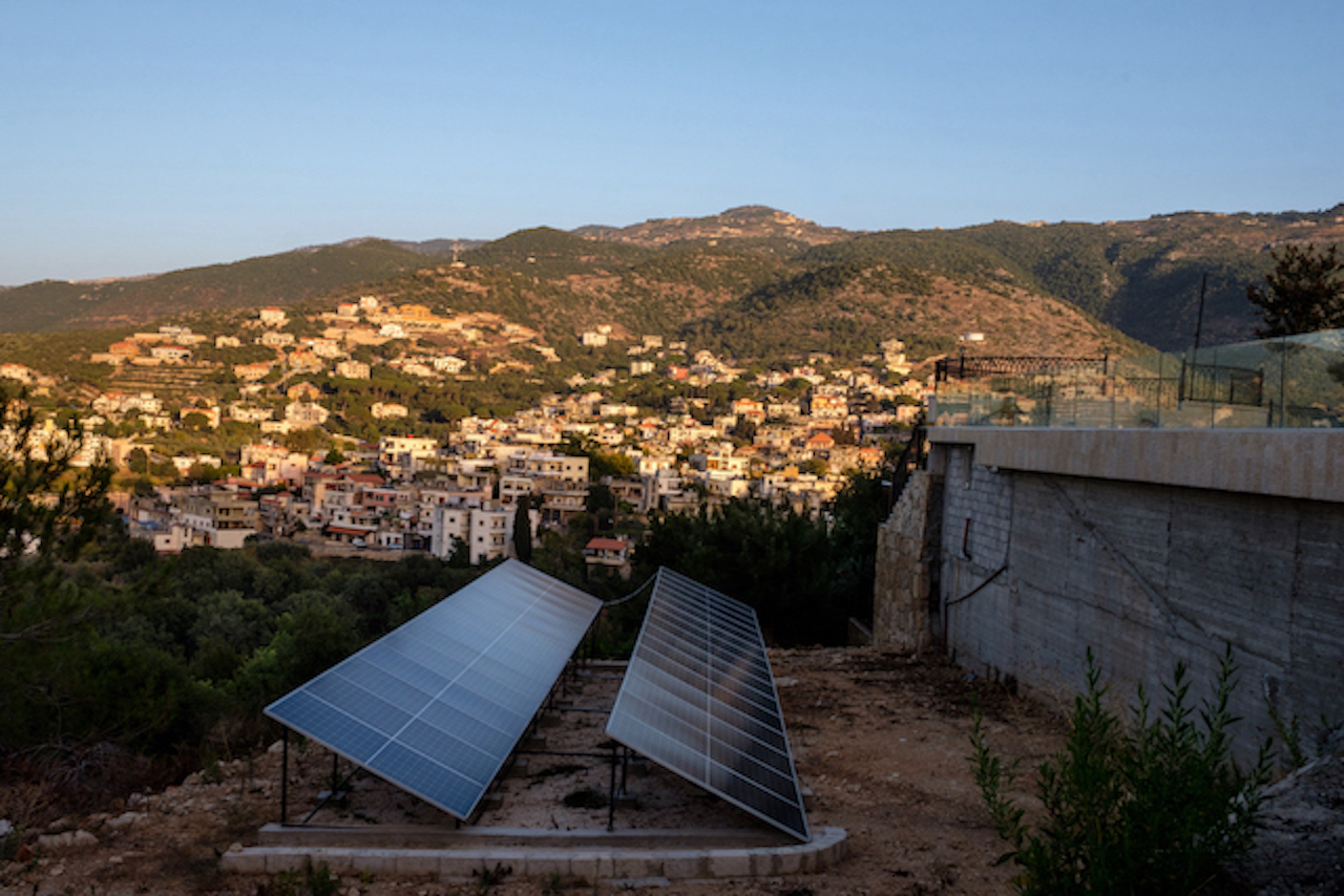 Two rows of solar panels installed on land surrounding villa that oversees a village. 