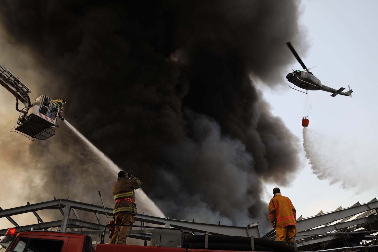 A Lebanese army helicopter, a firefighter on a mechanical ladder, and two firefighters on the ground work on extinguishing the fire that broke out at the port, one month after the August 4 explosion. 