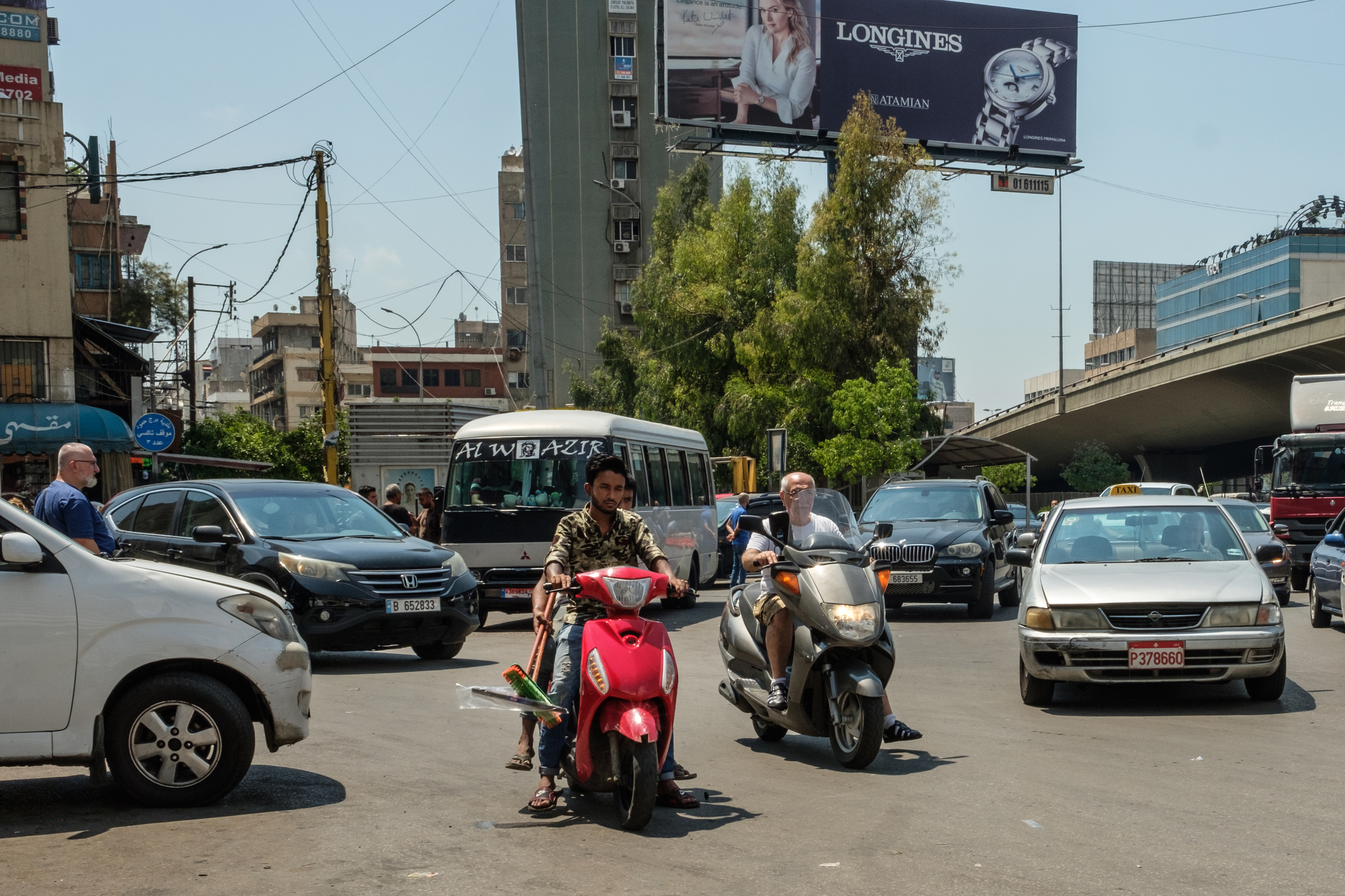 A bunch of cars and motorcycles drive around the Dawra roundabout