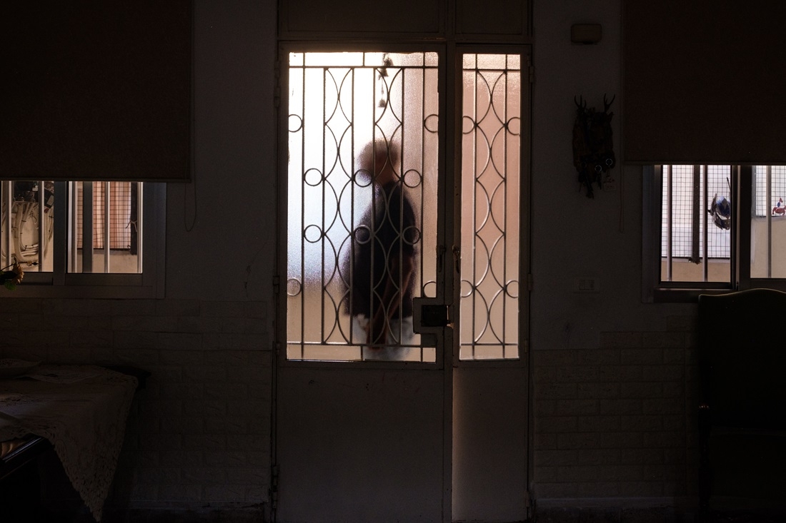 The silhouette of a man behind a glass door, from the inside of a dark living room.