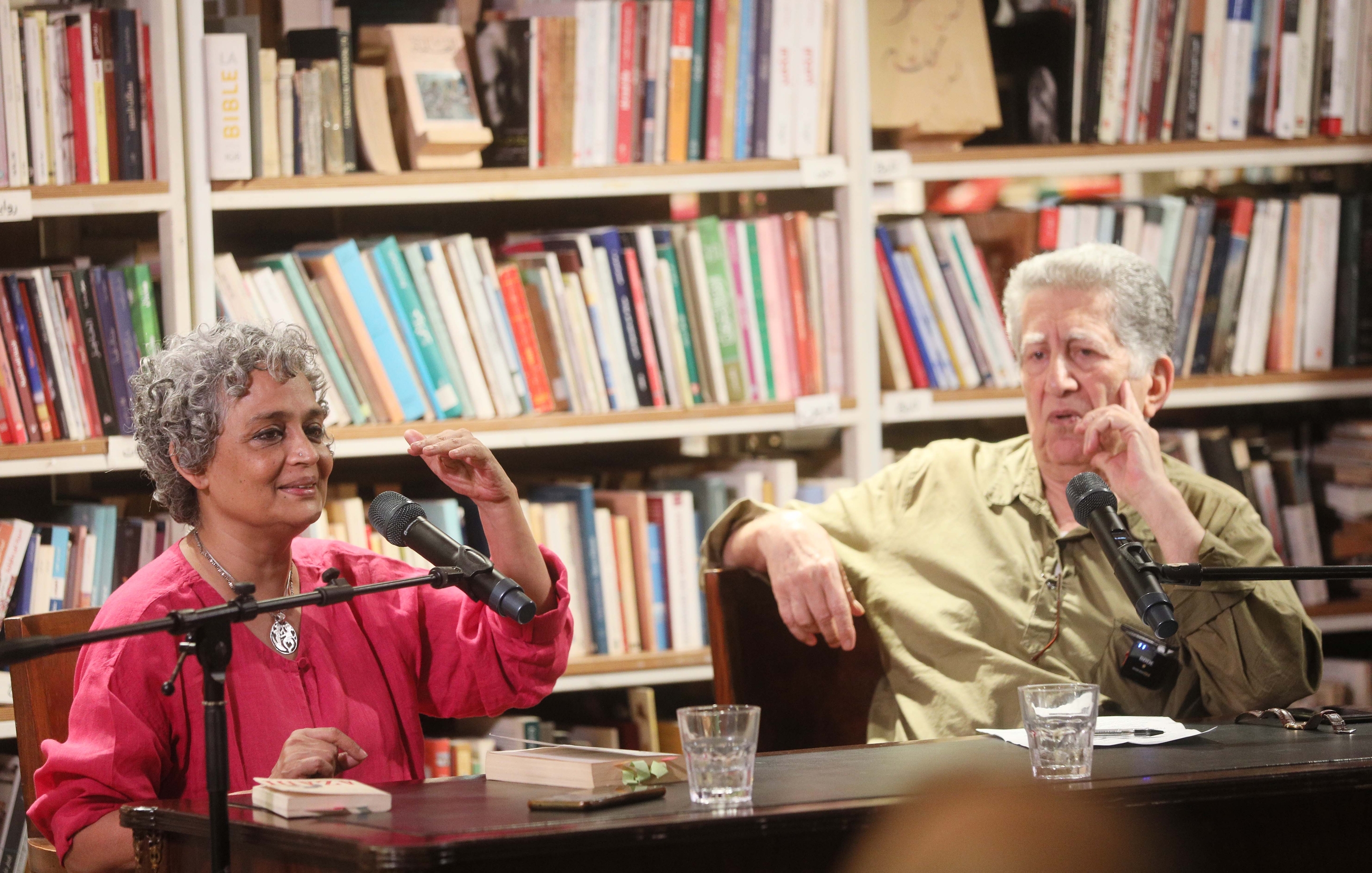 Indian author Arundhati Roy and Lebanese historian Fawwaz Traboulsi at Barzakh Bookshop, Hamra, with microphones in front of them and a stack of books behind. 