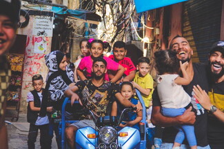 هاي الصورة في حي الصدمة اللي بنعتبره عاصمة شاتيلا. التكتك الكهربائي هو "الترند" الجديد لألعاب العيد، وصاحب التكتك بياخذ ألفين ليرة عالراكب وبيعملّه جولة بالمخيم مع أغاني وهتافات مثل "يا ولاد الكوكو يلعن أبوكو".
